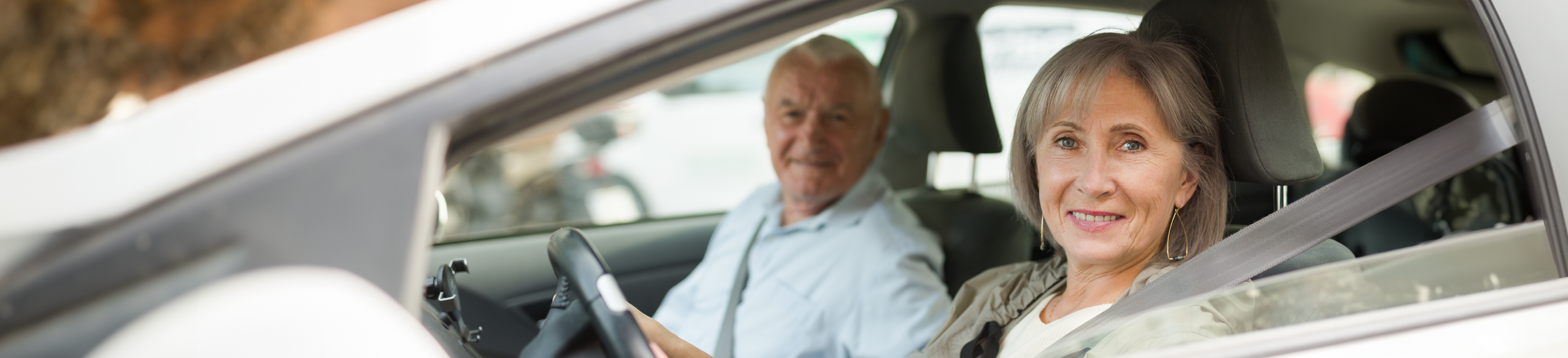image of older woman driving a car with her seatbelt on with a male passenger